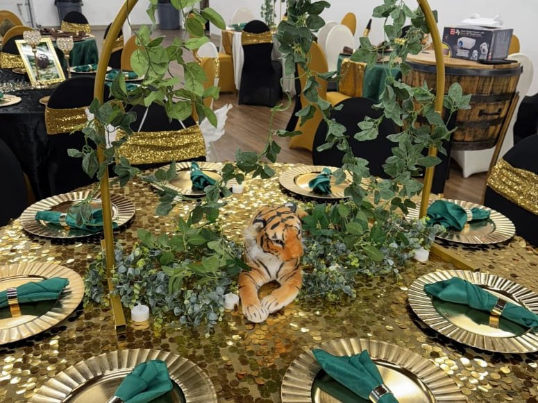 Safari-themed table with a gold sequin tablecloth, greenery garland and a plush tiger centerpiece