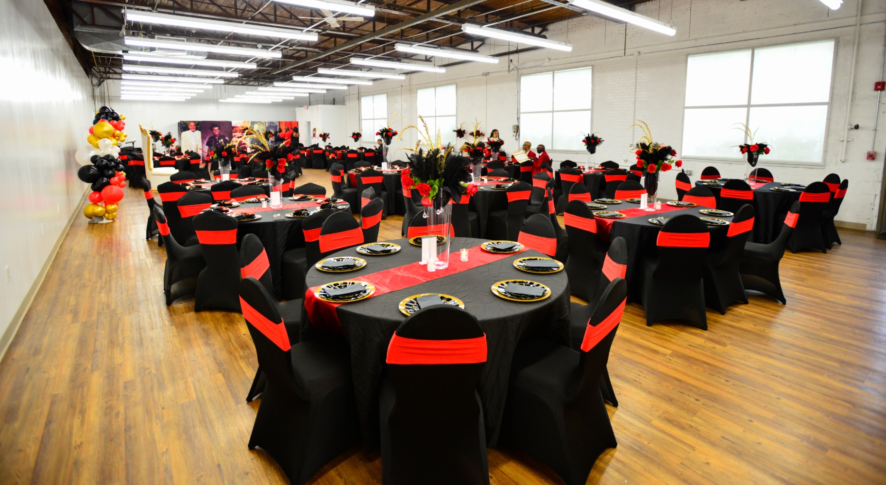Banquet hall filled with round tables dressed in black linens and red chair sashes